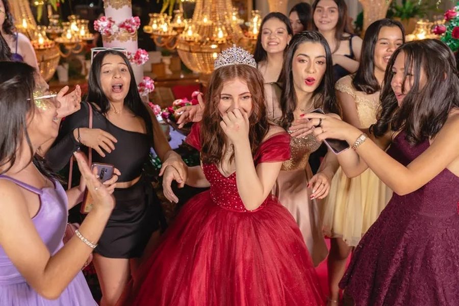 Quinceañera celebrando con su corte frente al pastel y los candelabros del salón