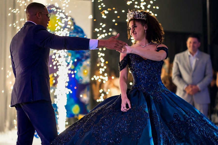 Quinceañera con vestido azul bailando el vals con su padrino entre luces de chispas